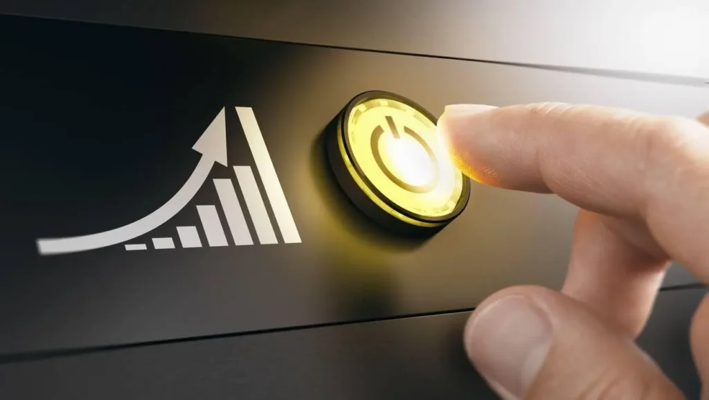 Un dedo presiona un botón amarillo iluminado, simbolizando encendido, con un gráfico de barras en crecimiento junto a una flecha ascendente, representando progreso, éxito y activación del crecimiento.